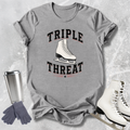 Gray t-shirt with 'Triple Threat' graphic, ice skates, gloves, and tumbler on a textured surface