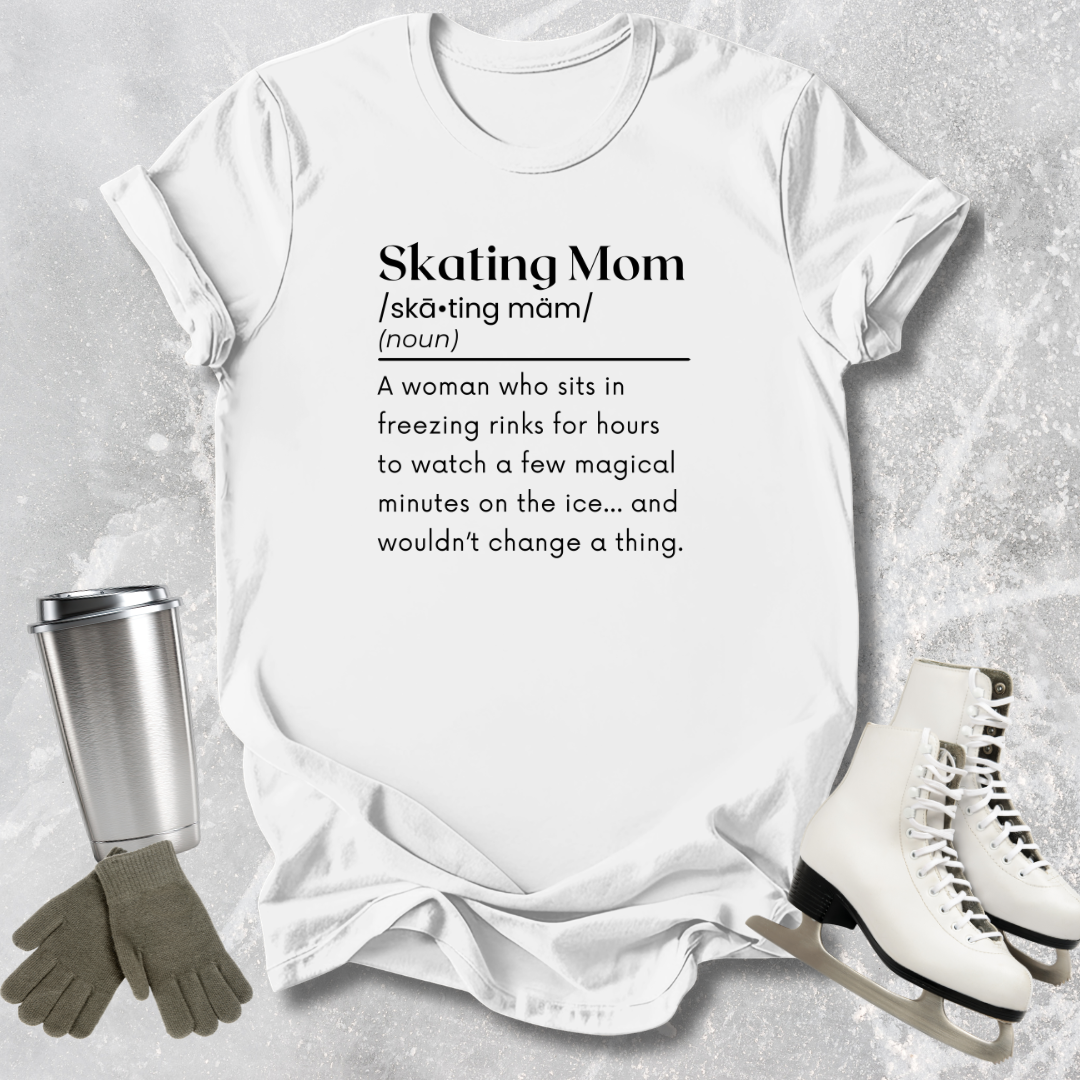 White t-shirt with 'Skating Mom' definition text, surrounded by ice skates, gloves, and a tumbler on a textured surface.