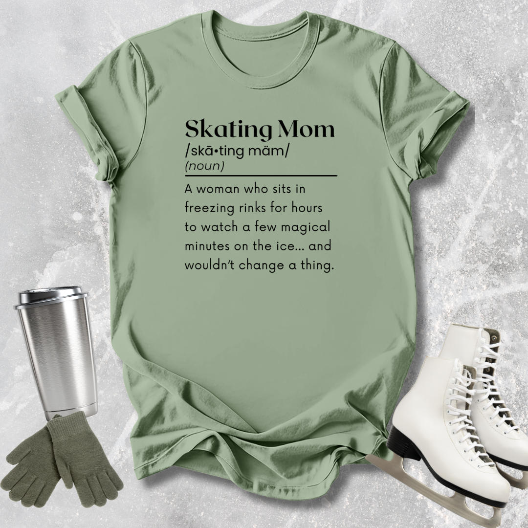 Green t-shirt with 'Skating Mom' definition text, placed on a textured surface with ice skates and a tumbler.