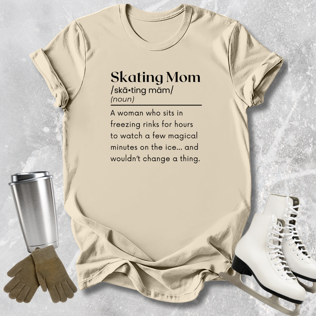 Beige t-shirt with 'Skating Mom' definition text, placed on a textured surface with ice skates and gloves.
