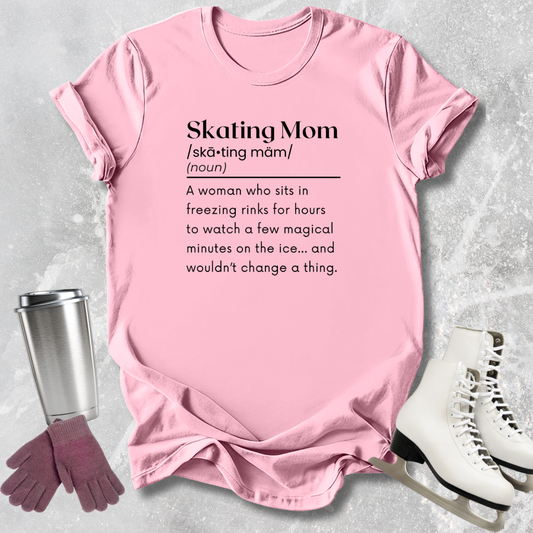 Pink t-shirt with 'Skating Mom' definition text, placed on a textured surface with a tumbler, gloves, and skates.