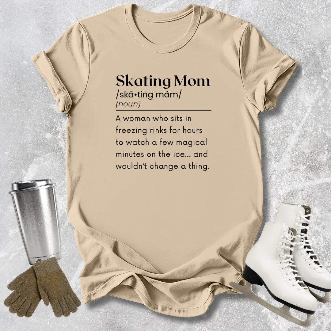 Beige t-shirt with 'Skating Mom' definition text, placed on a textured surface with ice skates and gloves.