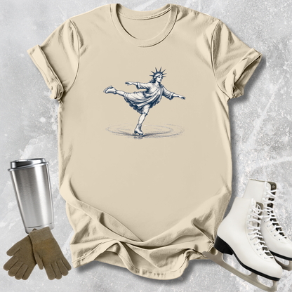 Beige t-shirt with a graphic of the Statue of Liberty, placed on a textured surface with a tumbler, gloves, and skates.