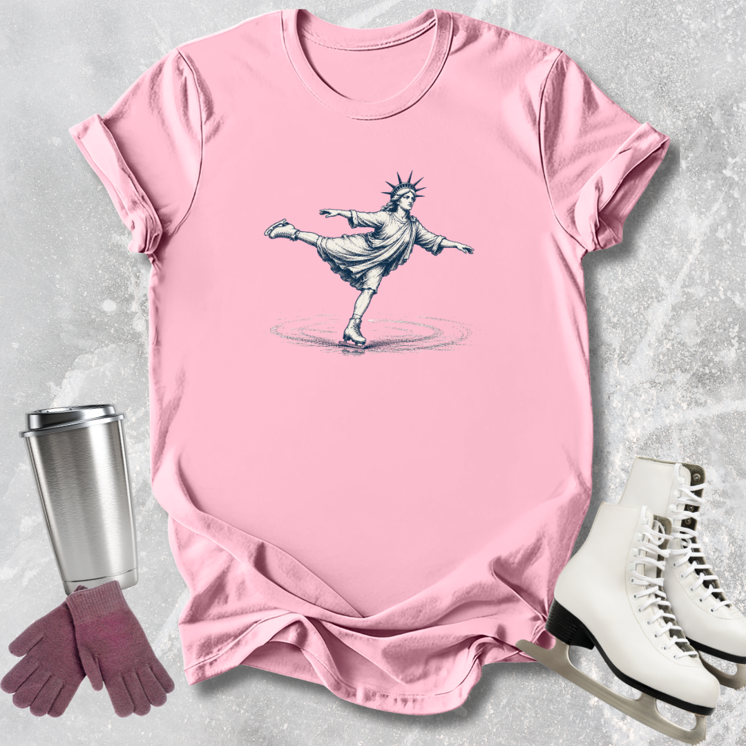 Pink t-shirt with a graphic design of the Statue of Liberty, placed on a textured surface with a tumbler, gloves, and skates.