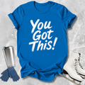 Blue t-shirt with 'You Got This!' text, silver tumbler, blue gloves, and white skates on a textured gray background