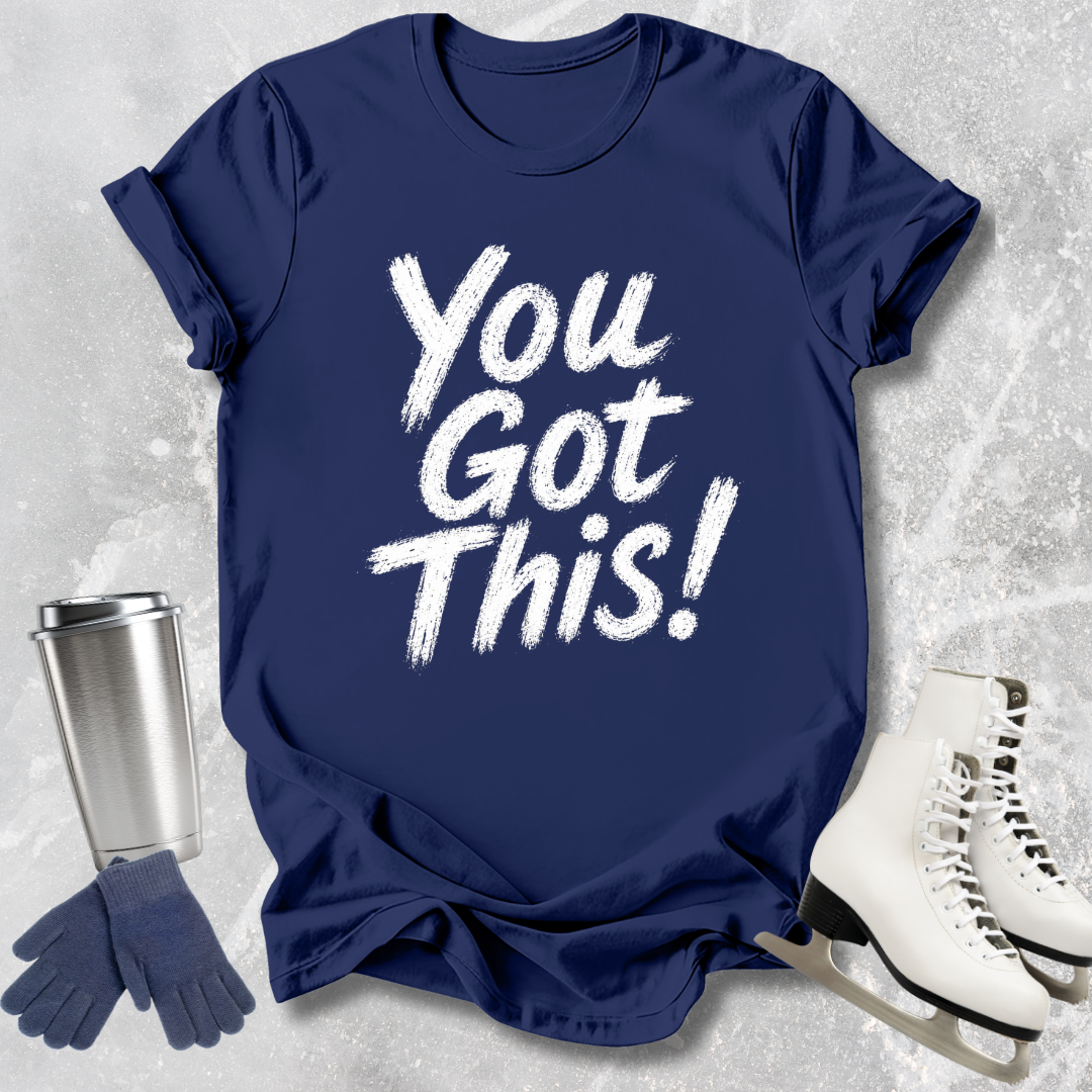 Navy blue t-shirt with 'You Got This!' text, silver tumbler, gloves, and white skates on a textured gray background