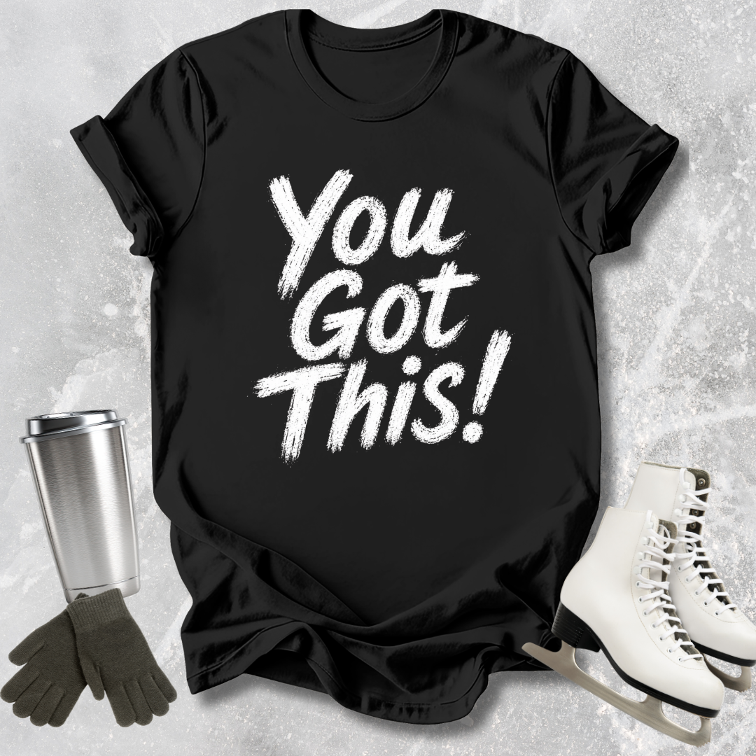 Black t-shirt with 'You Got This!' text, next to a silver tumbler, black gloves, and white skates on a textured surface.