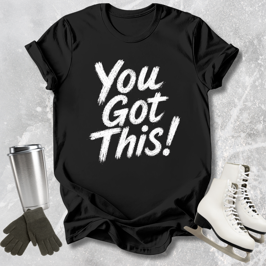 Black t-shirt with 'You Got This!' text, next to a silver tumbler, black gloves, and white skates on a textured surface.