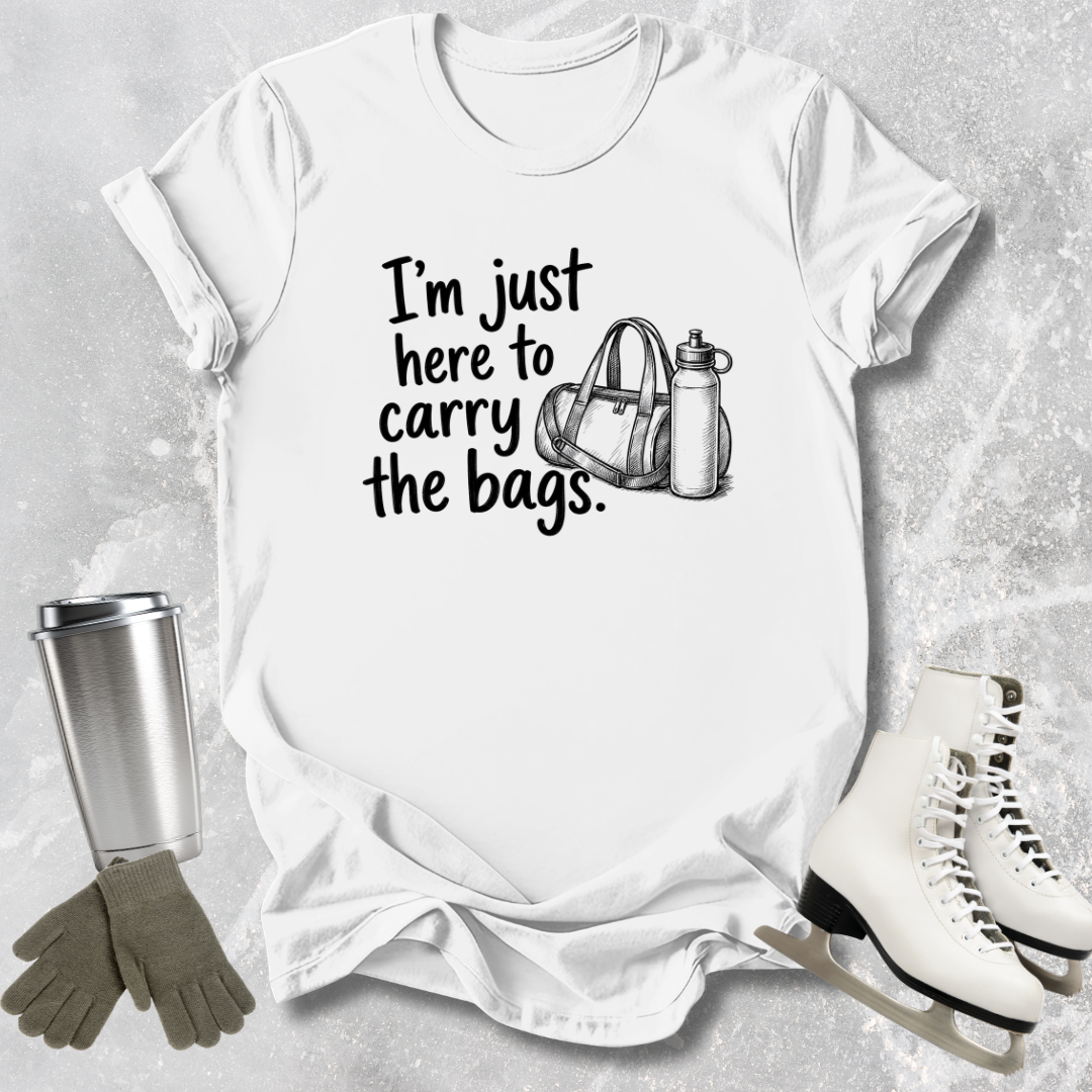White t-shirt with text 'I'm just here to carry the bags' on a textured surface with accessories.