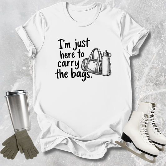 White t-shirt with text 'I'm just here to carry the bags' on a textured surface with accessories.