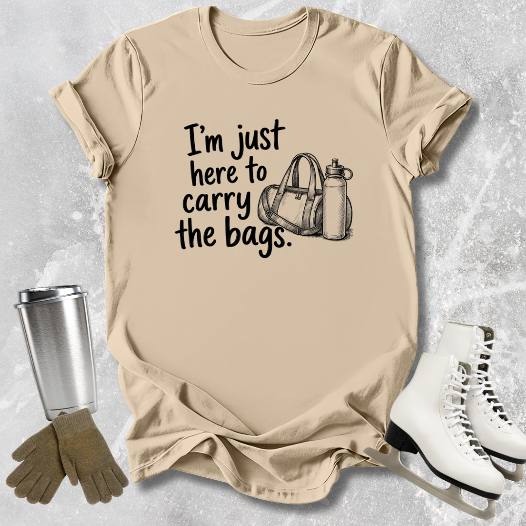 Beige -tshirt with text 'I'm just here to carry the bags' on a textured surface with accessories.