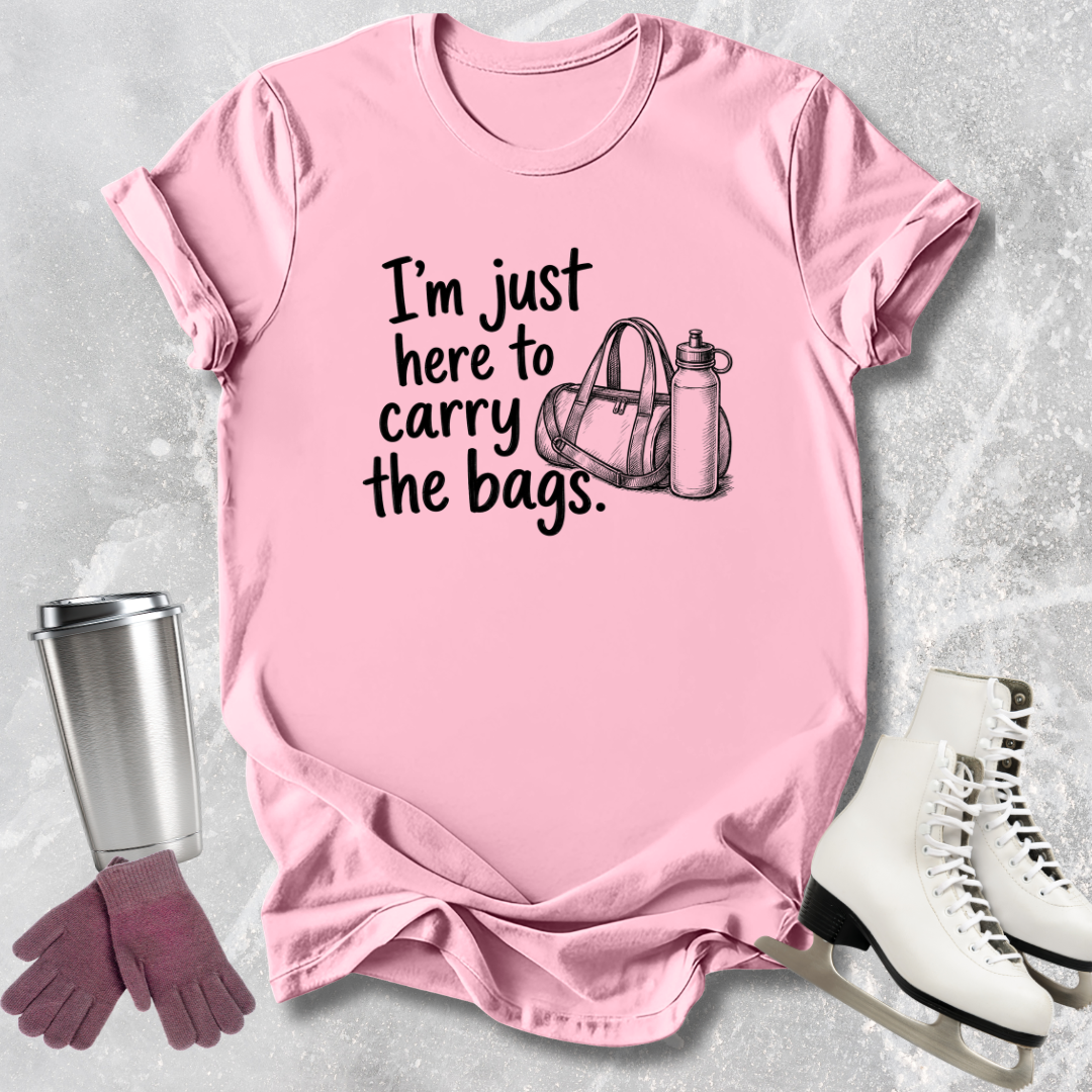 Pink t-shirt with text 'I'm just here to carry the bags' on a textured surface with accessories.