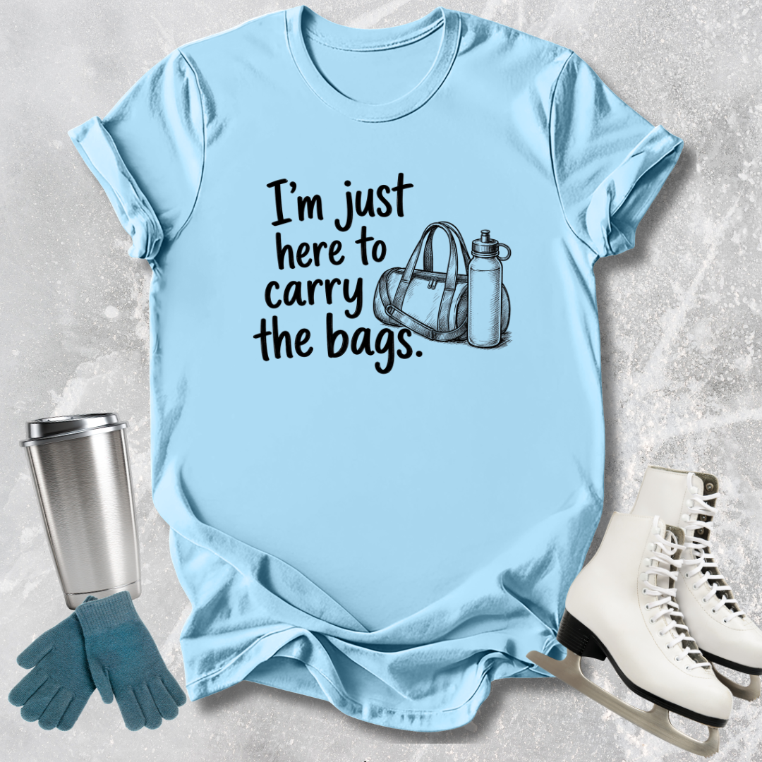 Light blue -shirt with text 'I'm just here to carry the bags' on a textured surface with accessories.