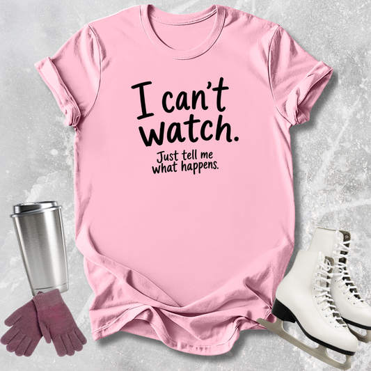 Pink t-shirt with text 'I can't watch. Just tell me what happens.' on a textured surface with a tumbler, gloves, and skates.