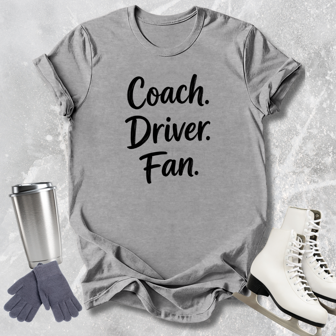 Gray t-shirt with 'Coach. Driver. Fan.' text, next to a silver tumbler, gray gloves, and white skates on a textured surface.