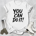 White t-shirt with 'You Can Do It!' text, silver tumbler, gray gloves, and white skates on a light gray background
