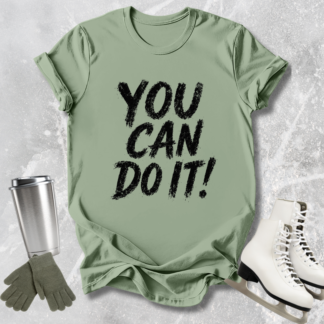 Green t-shirt with 'YOU CAN DO IT!' text, paired with a silver tumbler, green gloves, and white skates on a textured surface.