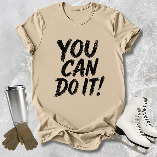 Beige t-shirt with 'You Can Do It!' text, next to a silver tumbler, brown gloves, and white skates on a light gray background.