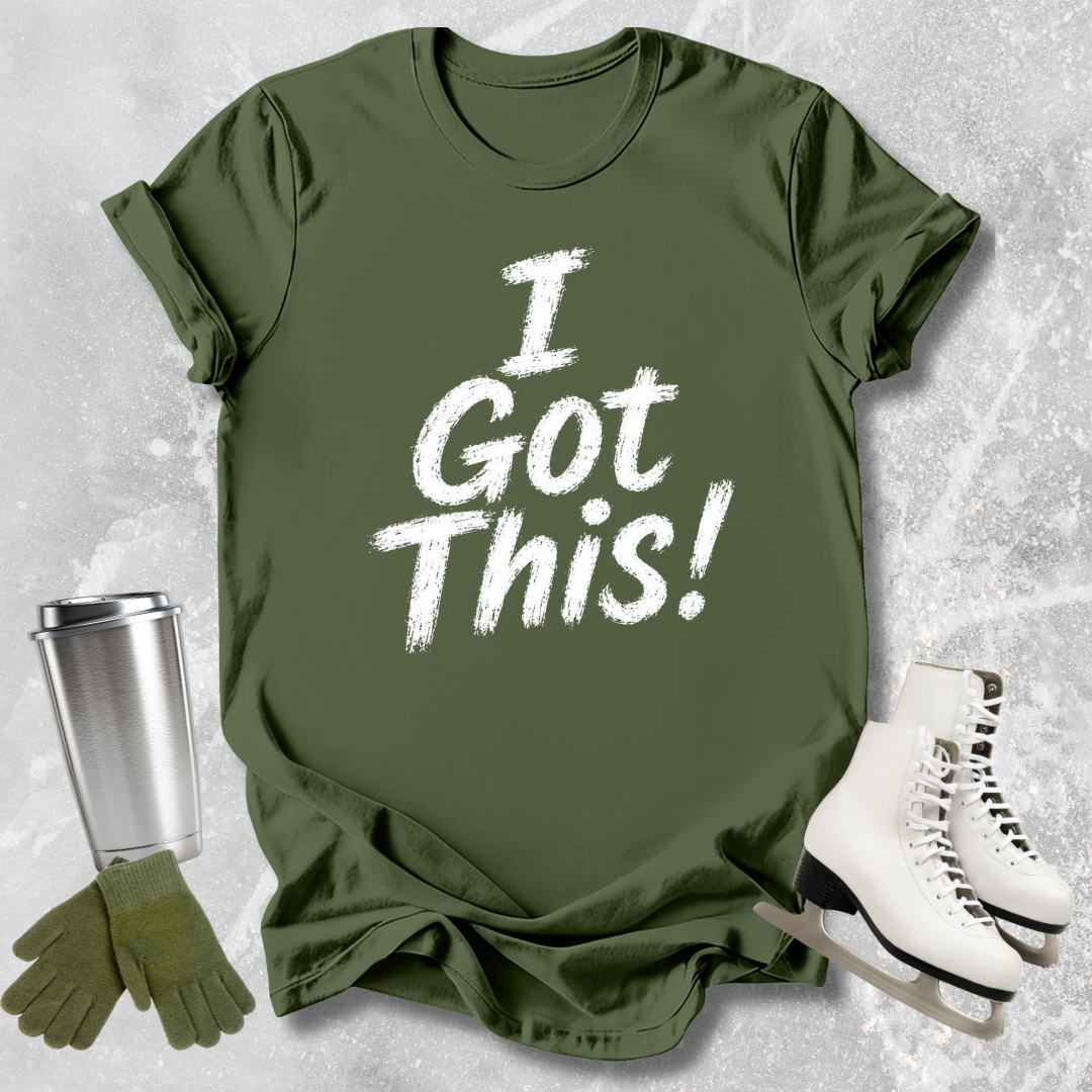 Green t-shirt with 'I Got This!' text, paired with a silver tumbler, green gloves, and white skates on a textured gray background.