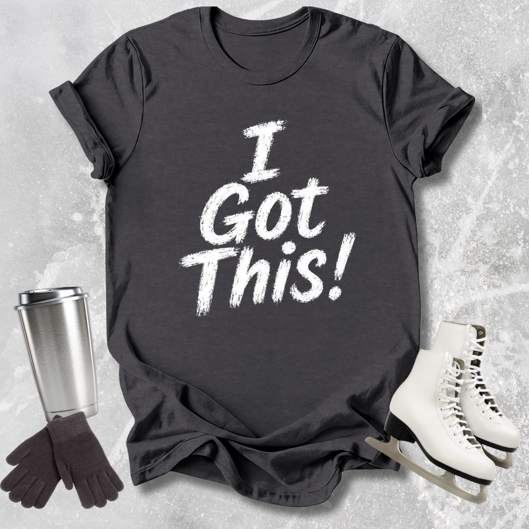 Black t-shirt with 'I Got This!' text, next to a silver tumbler, black gloves, and white skates on a textured surface.