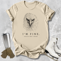 Beige t-shirt with an eagle graphic and text 'I'm fine. Skating mom' on a textured surface.