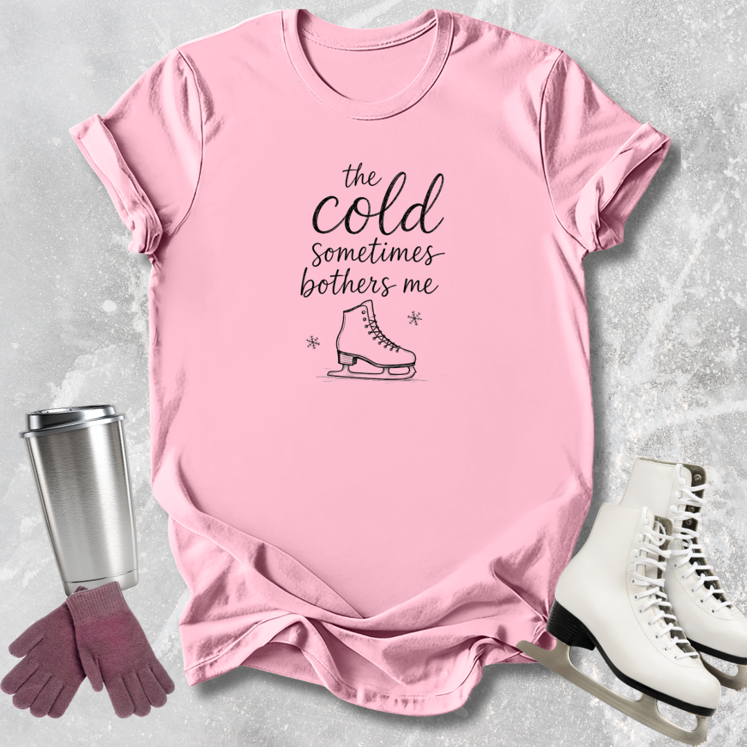 Pink t-shirt with text and graphics, next to a silver tumbler, pink gloves, and white skates on a light gray background.