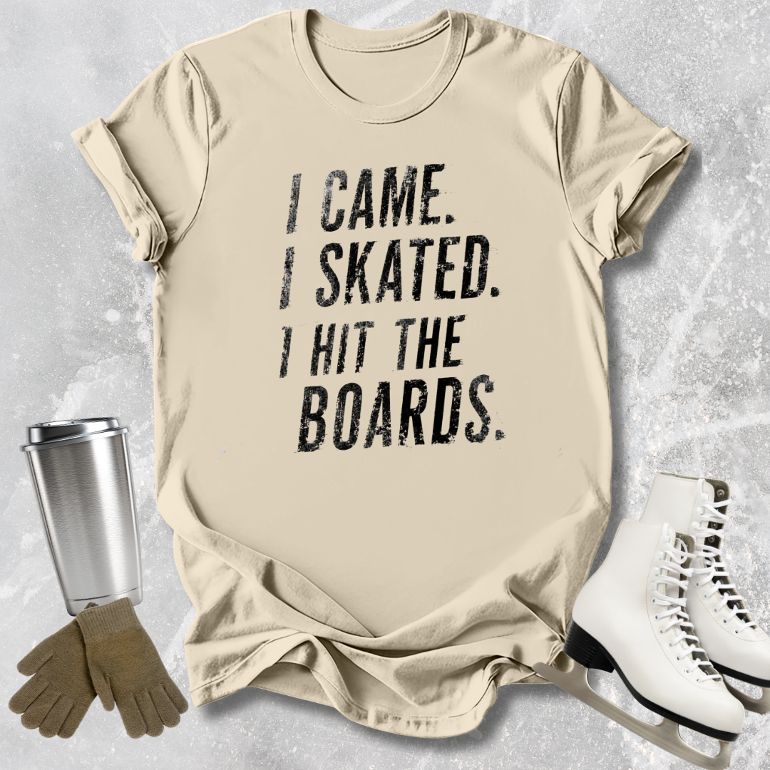 Beige t-shirt with 'I Came. I Skated. I Hit the Boards.' text, next to ice skates and a tumbler on a textured surface.