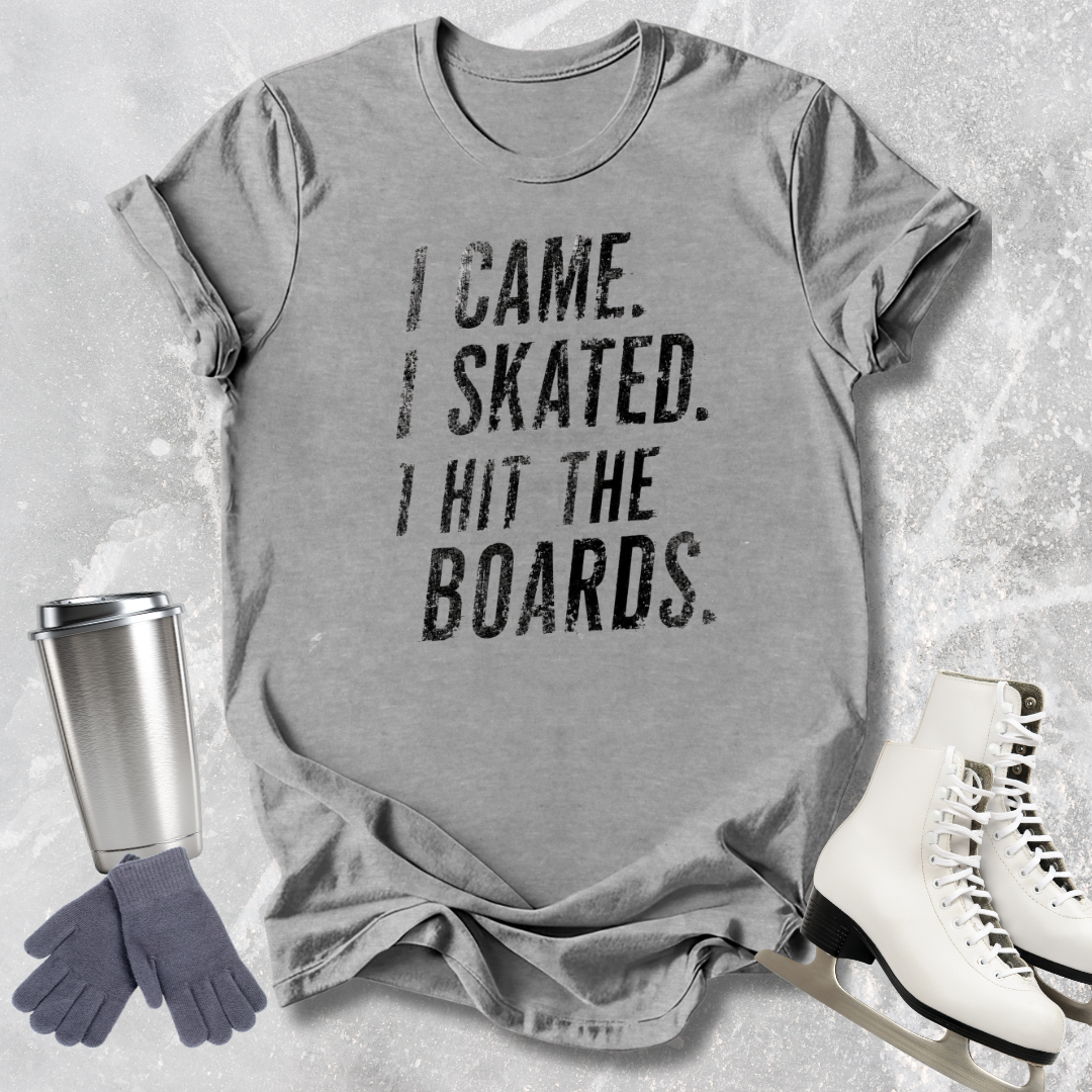 Gray t-shirt with 'I came. I skated. I hit the boards.' text, next to ice skates and a tumbler on a textured surface.