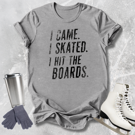 Gray t-shirt with 'I came. I skated. I hit the boards.' text, next to ice skates and a tumbler on a textured surface.
