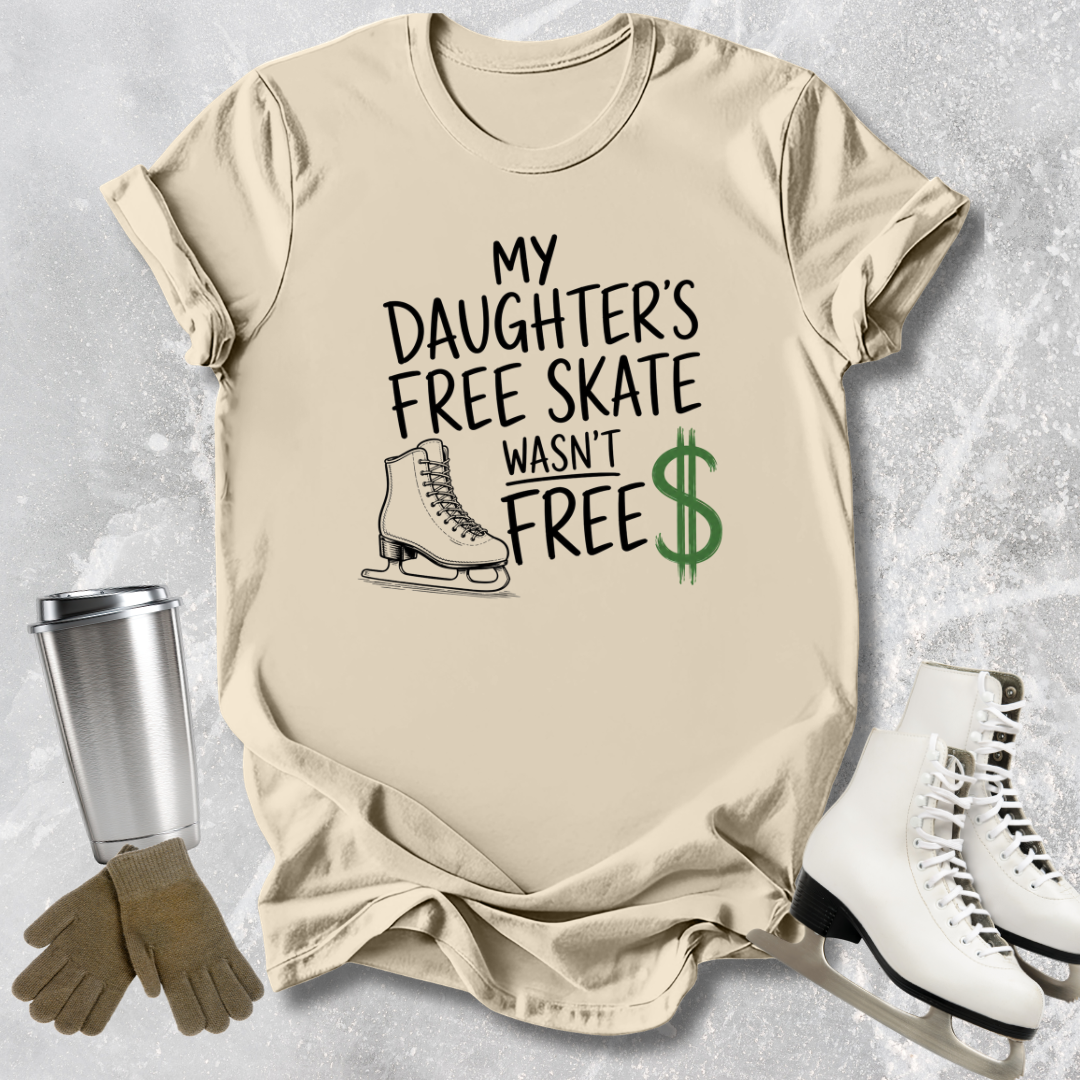 Beige t-shirt with text 'My daughter's free skate wasn't free' on a textured surface with ice skates and a tumbler.
