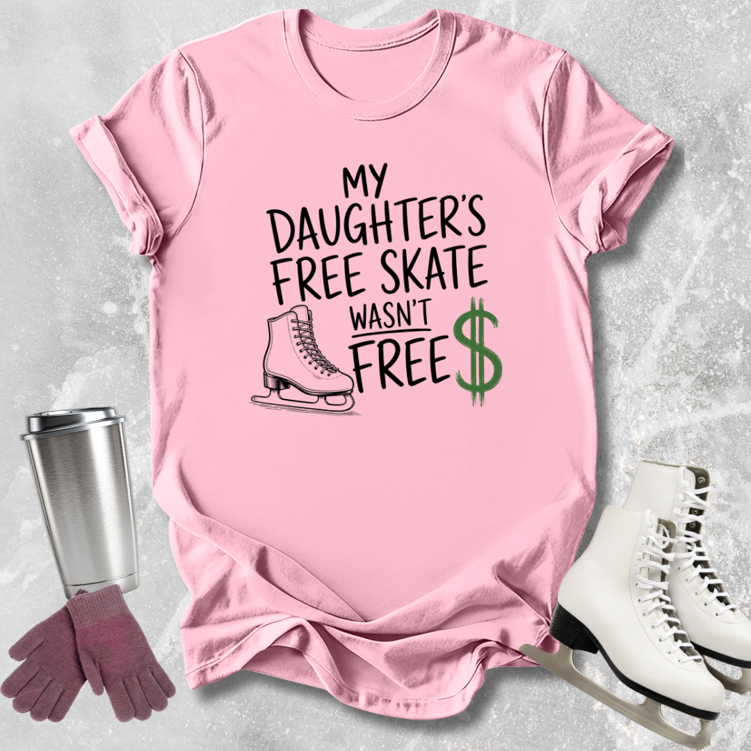 Pink t-shirt with text 'My daughter's free skate wasn't free' on a textured surface with ice skates and gloves.