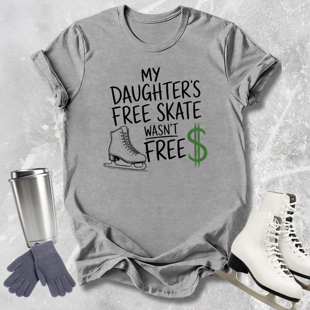 Gray t-shirt with text 'My Daughter's Free Skate Wasn't Free' on a textured surface with ice skates and a tumbler.