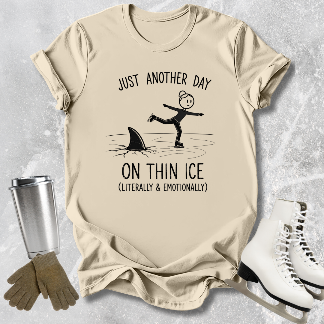 Beige t-shirt with humorous graphic and text, placed on a textured surface with accessories like a tumbler, gloves, and skates.