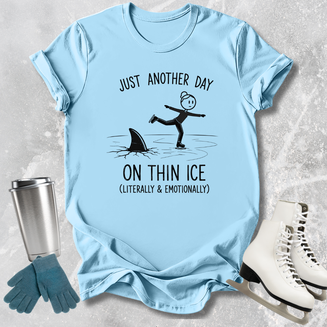 Light blue t-shirt with humorous graphic and text, placed on a textured surface with accessories like gloves and skates.
