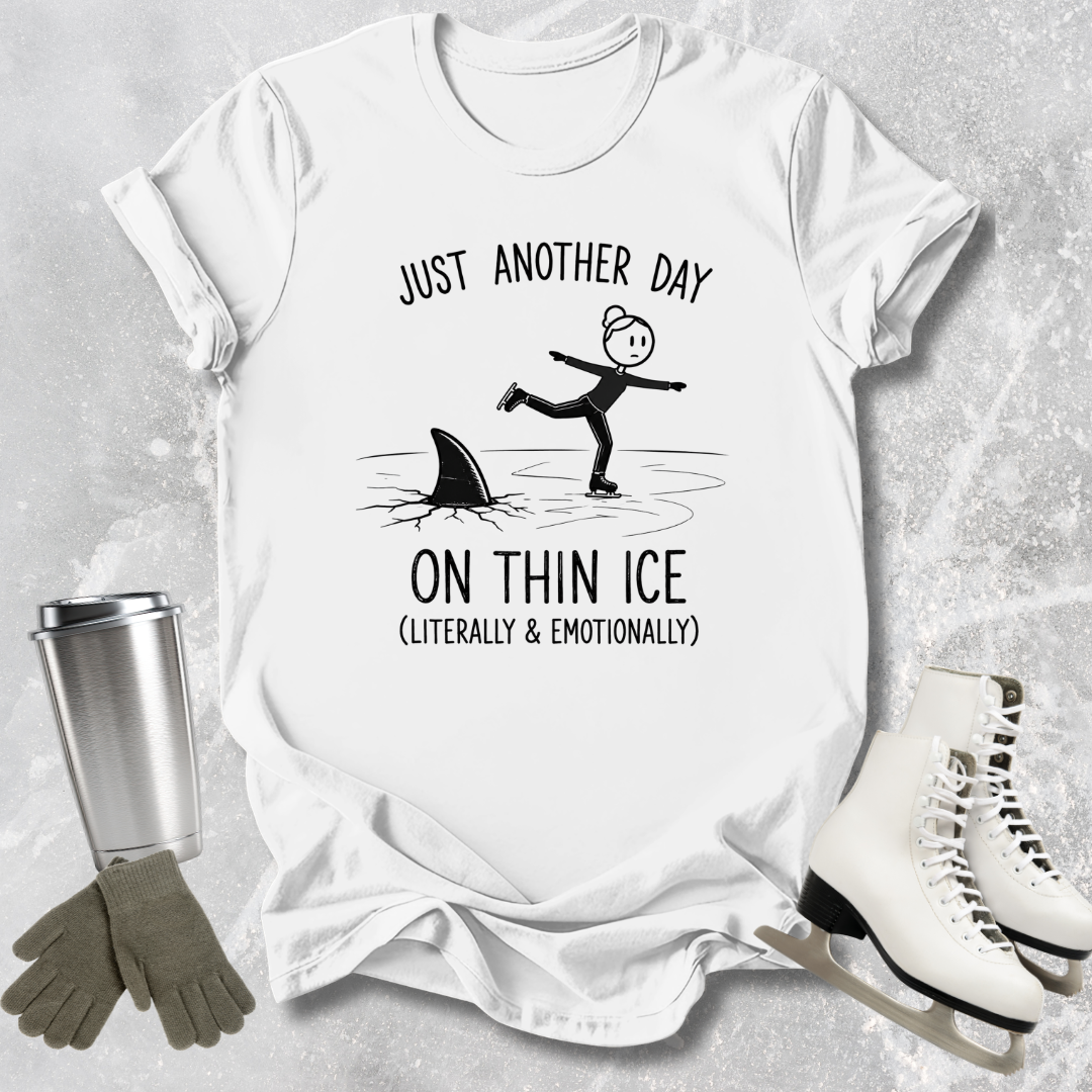 White t-shirt with humorous graphic and text, surrounded by ice skates, gloves, and a tumbler on a textured surface.