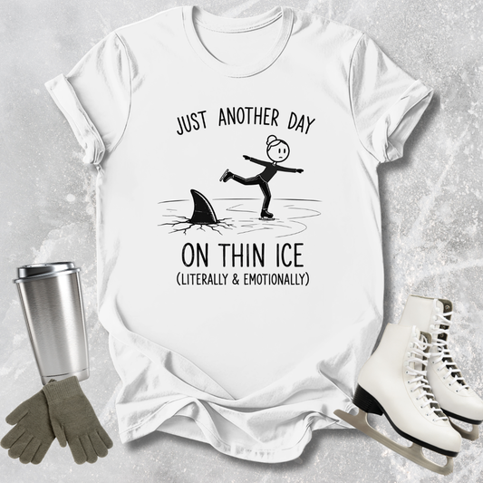 White t-shirt with humorous graphic and text, surrounded by ice skates, gloves, and a tumbler on a textured surface.