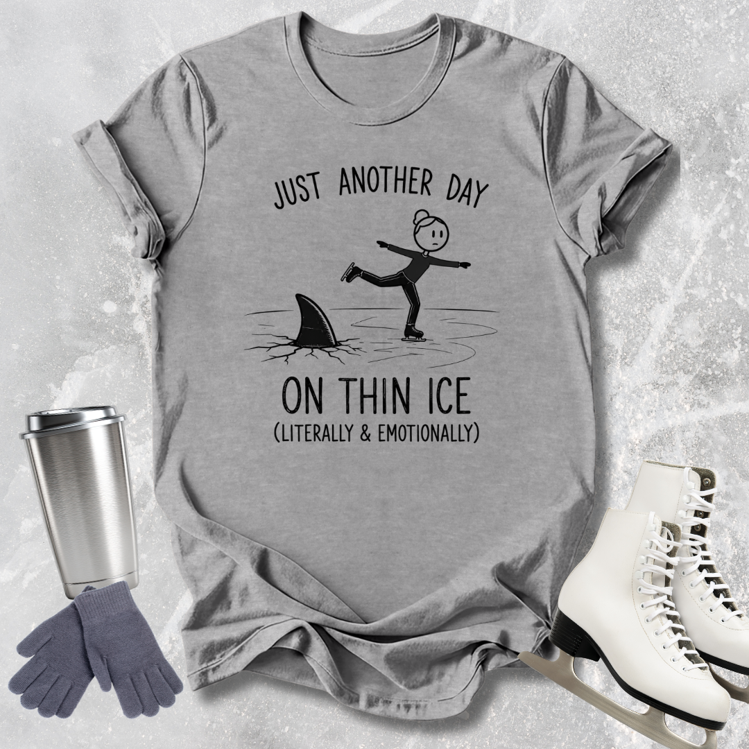 Gray t-shirt with a humorous graphic and text, placed on a textured surface with a tumbler, gloves, and skates.