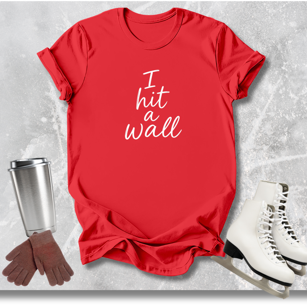 Red t-shirt with 'I hit a wall' text, white skates, silver tumbler, and brown gloves on a textured gray background