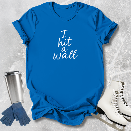 Blue t-shirt with 'I hit a wall' text, silver tumbler, blue gloves, and white skates on a textured gray background
