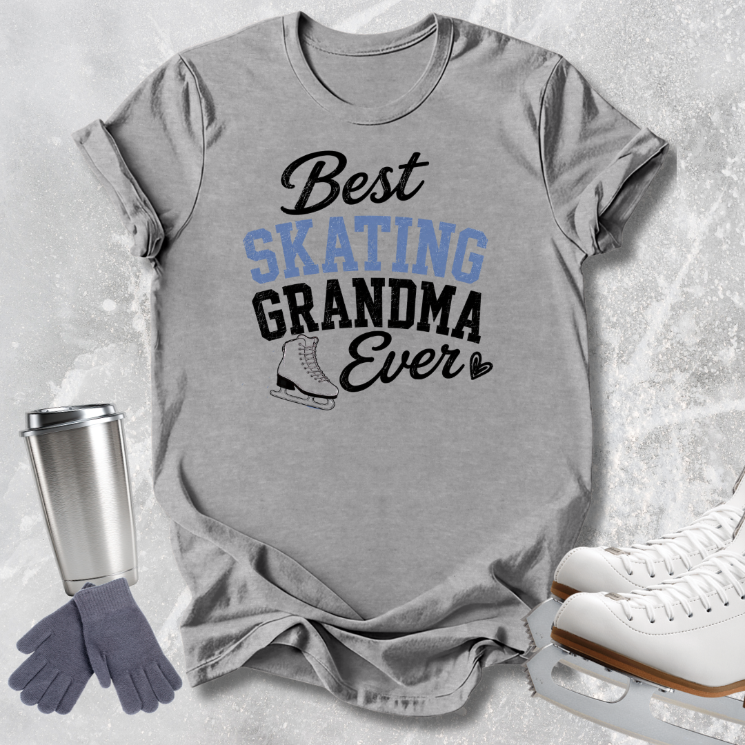 A heather gray graphic t-shirt featuring the text 'Best SKATING GRANDMA Ever' in black and light blue, styled in a flat-lay with ice skates, gloves, and a travel tumbler on a textured light gray background.
