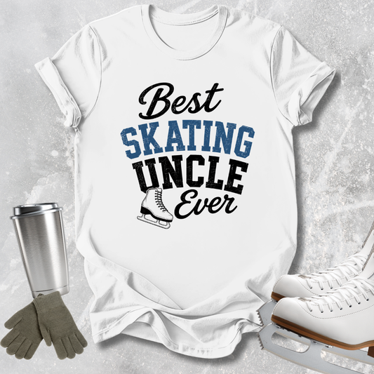 white graphic T-shirt laid flat on a light gray textured surface, with the text 'Best SKATING UNCLE Ever' in black and blue lettering and a small ice skate illustration. Surrounding props include a silver tumbler, tan gloves, and white ice skates.