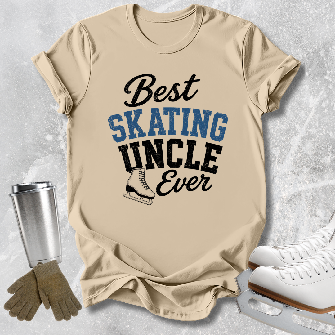 A beige graphic T-shirt laid flat on a light gray textured background, with the text 'Best SKATING UNCLE Ever' in black and blue lettering and a small ice skate illustration. White ice skates, tan gloves, and a metal travel tumbler are arranged around the shirt as styling props.