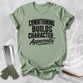A sage green graphic t-shirt with the text 'CONDITIONING BUILDS CHARACTER.