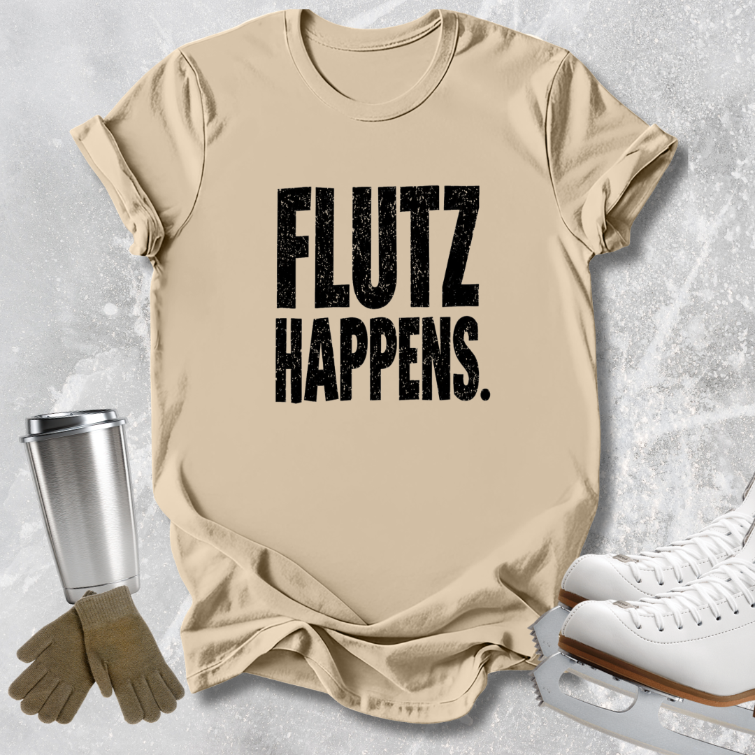 A beige graphic t-shirt with the text 'FLUTZ HAPPENS.' printed in distressed black letters, styled in a flat-lay with ice skating shoes, gloves, and a travel tumbler on a textured gray background.