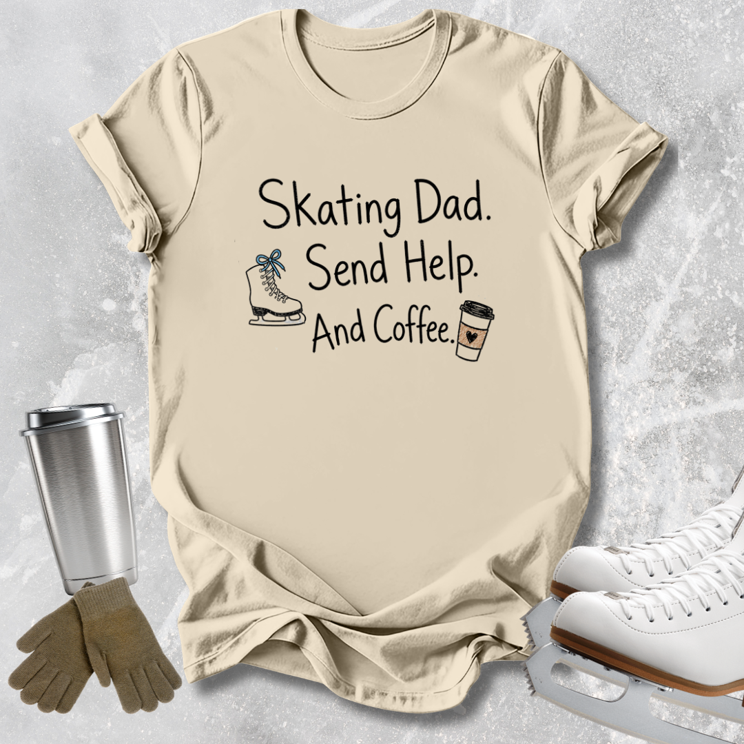 A beige graphic t-shirt laid flat on a light gray textured background, surrounded by ice skating props including white ice skates, a metal travel mug, and a pair of brown gloves. The t-shirt features the text 'Skating Dad.