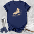 A navy blue short-sleeve T-shirt laid flat on a light gray textured surface, featuring a distressed beige ice skate graphic on the chest. Surrounding the shirt are white ice skates, navy gloves, and a stainless steel travel mug.