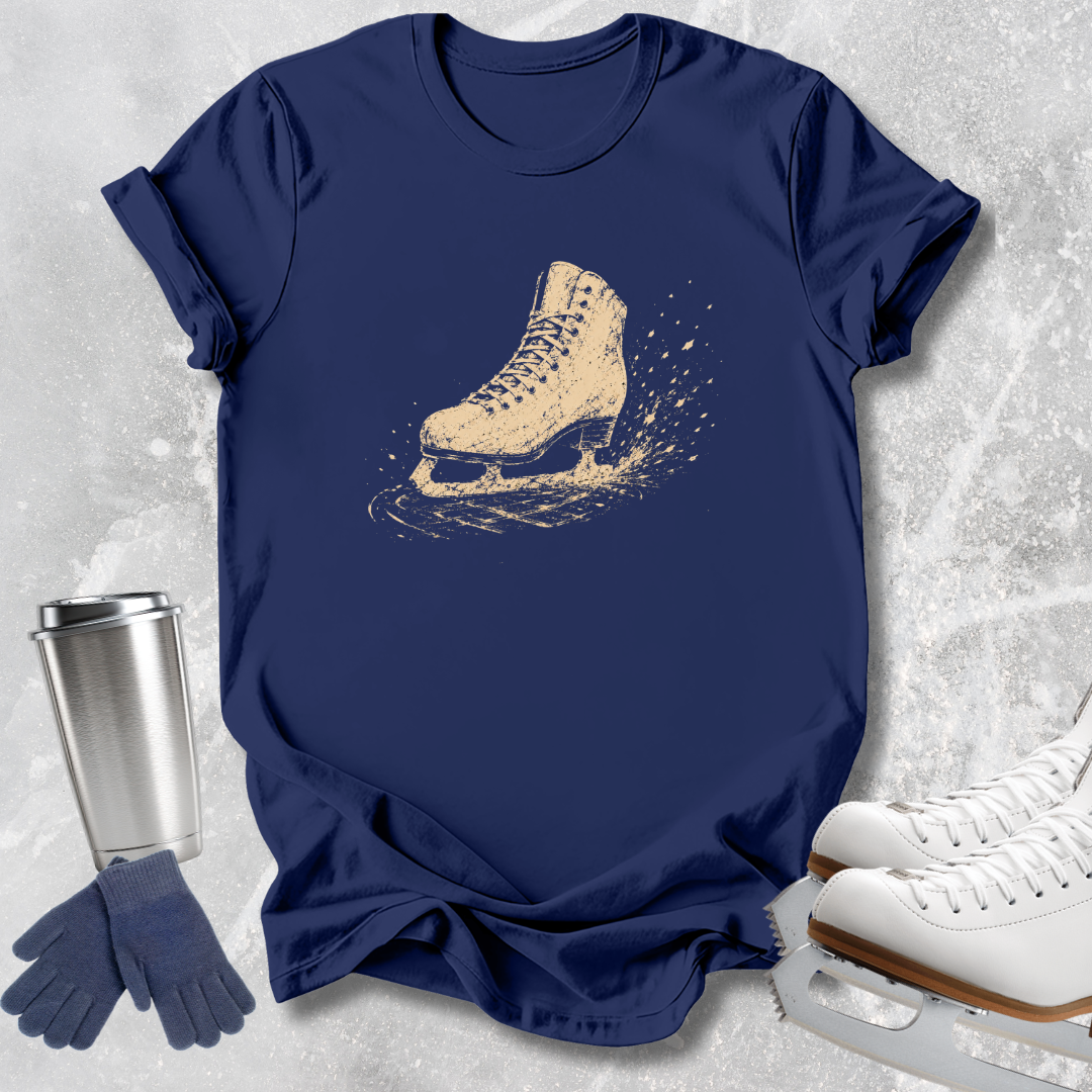 A navy blue short-sleeve T-shirt laid flat on a light gray textured surface, featuring a distressed beige ice skate graphic on the chest. Surrounding the shirt are white ice skates, navy gloves, and a stainless steel travel mug.