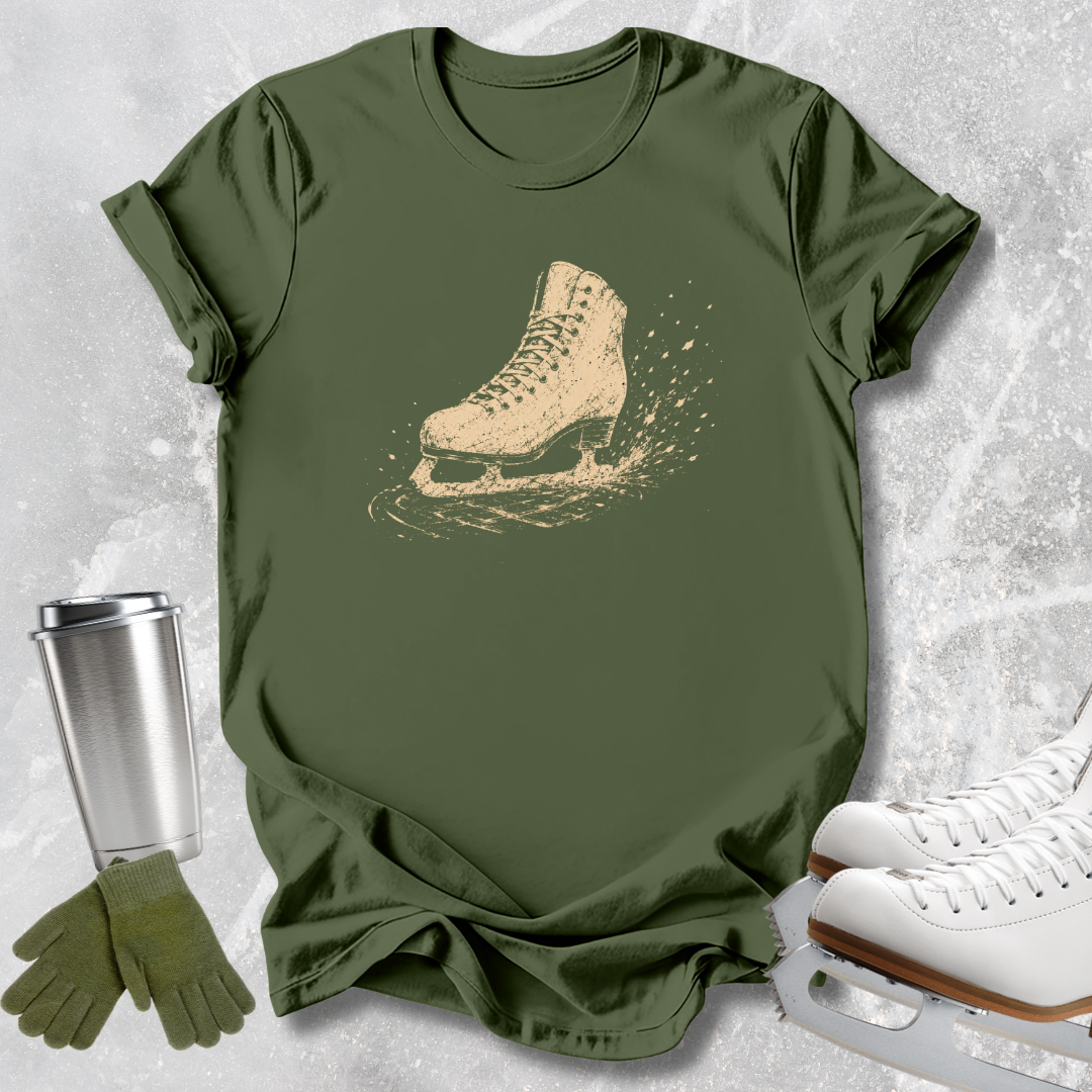 An olive green graphic t-shirt featuring a distressed beige ice skate print, styled in a flat-lay arrangement with white ice skates, green gloves, and a silver tumbler on a textured light gray background.
