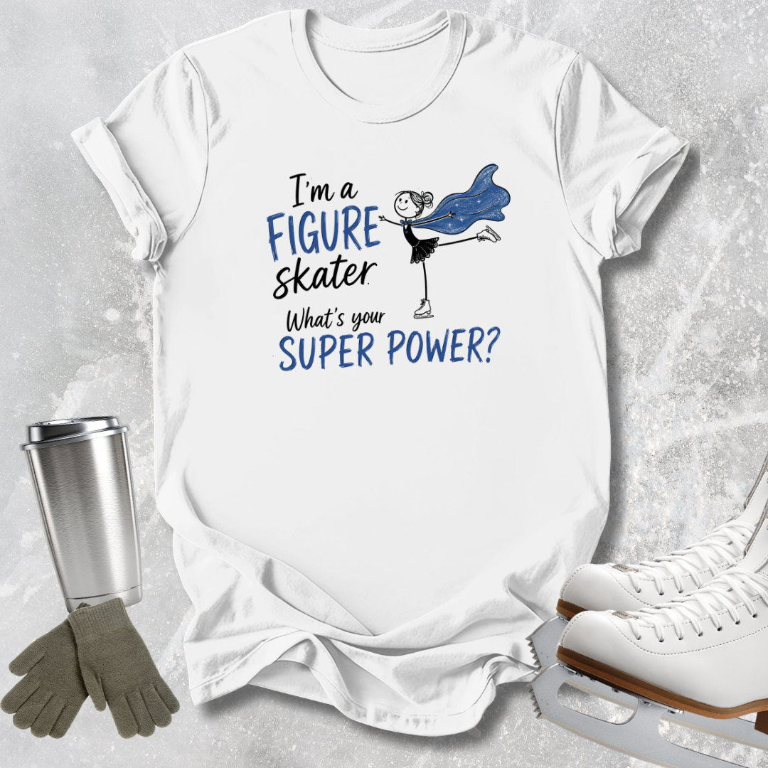 A white graphic T-shirt laid flat on a light gray textured surface, with a printed design that reads 'I'm a FIGURE skater What's your SUPER POWER?' in black and blue text, alongside a simple figure skater illustration. Ice skates, gloves, and a metal tumbler are placed around the shirt as styled props.