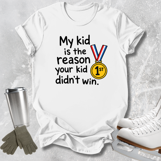 A white short-sleeve T-shirt laid flat on a light gray textured surface, printed with the phrase 'My kid is the reason your kid didn't win.' in black text and a gold medal graphic with red, white, and blue ribbon.